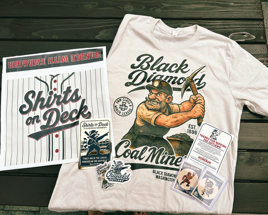 Flat lay of a Shirts On Deck Founding Member package featuring a Black Diamond Coal Miners t-shirt, trading cards, foil membership card, sticker pack, and printed insert on a wooden surface.