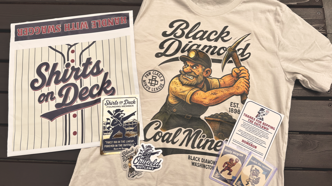 Flat lay of a Shirts On Deck Founding Member package featuring a Black Diamond Coal Miners t-shirt, trading cards, foil membership card, sticker pack, and printed insert on a wooden surface.