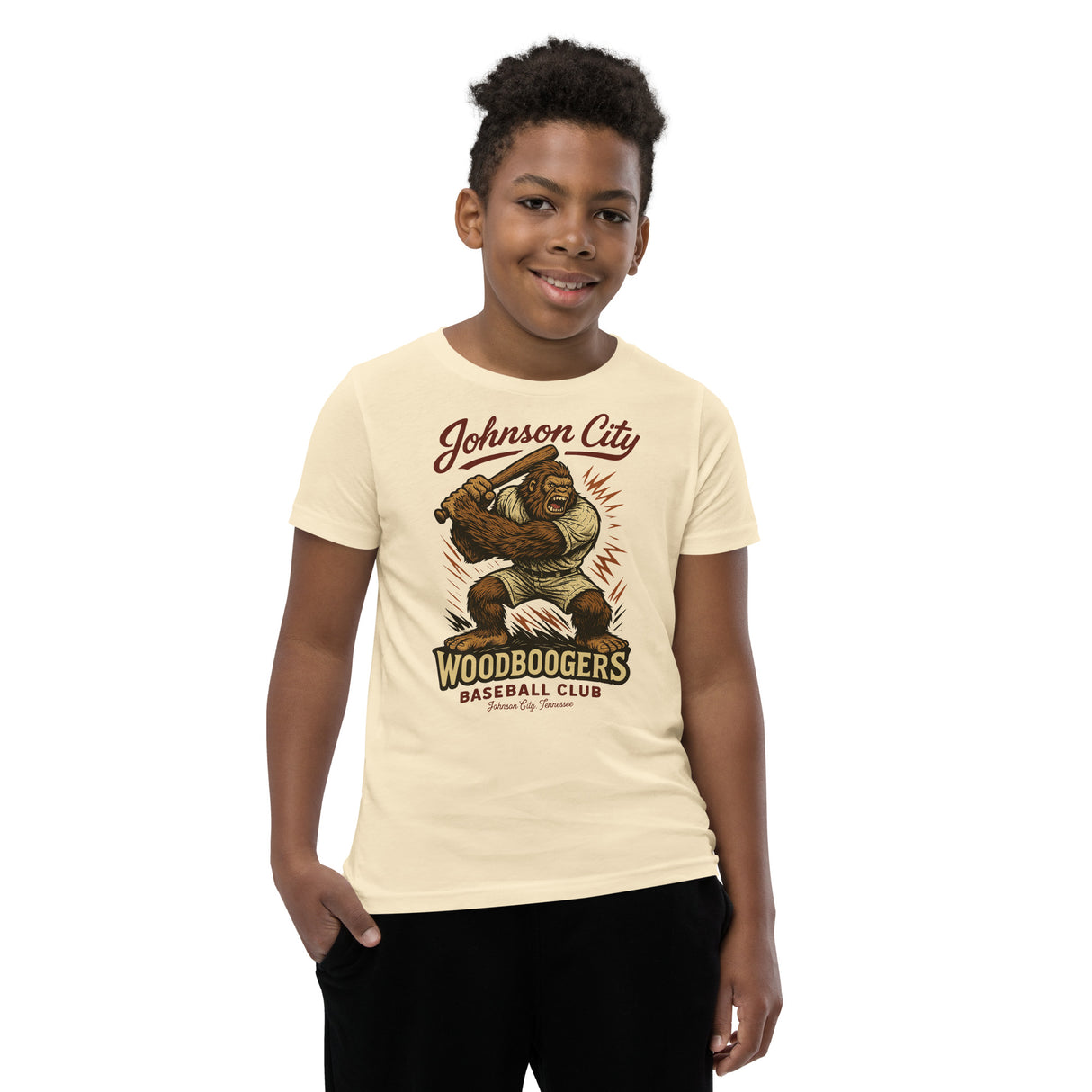 Youth boy model wearing Johnson City Woodboogers Bigfoot mascot tee in natural Bella Canvas 3001Y shirt