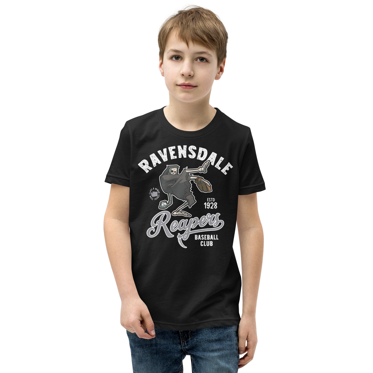 Young boy modeling the Ravensdale Reapers youth baseball t-shirt in black, featuring a vintage grim reaper mascot from a fictional minor league team.