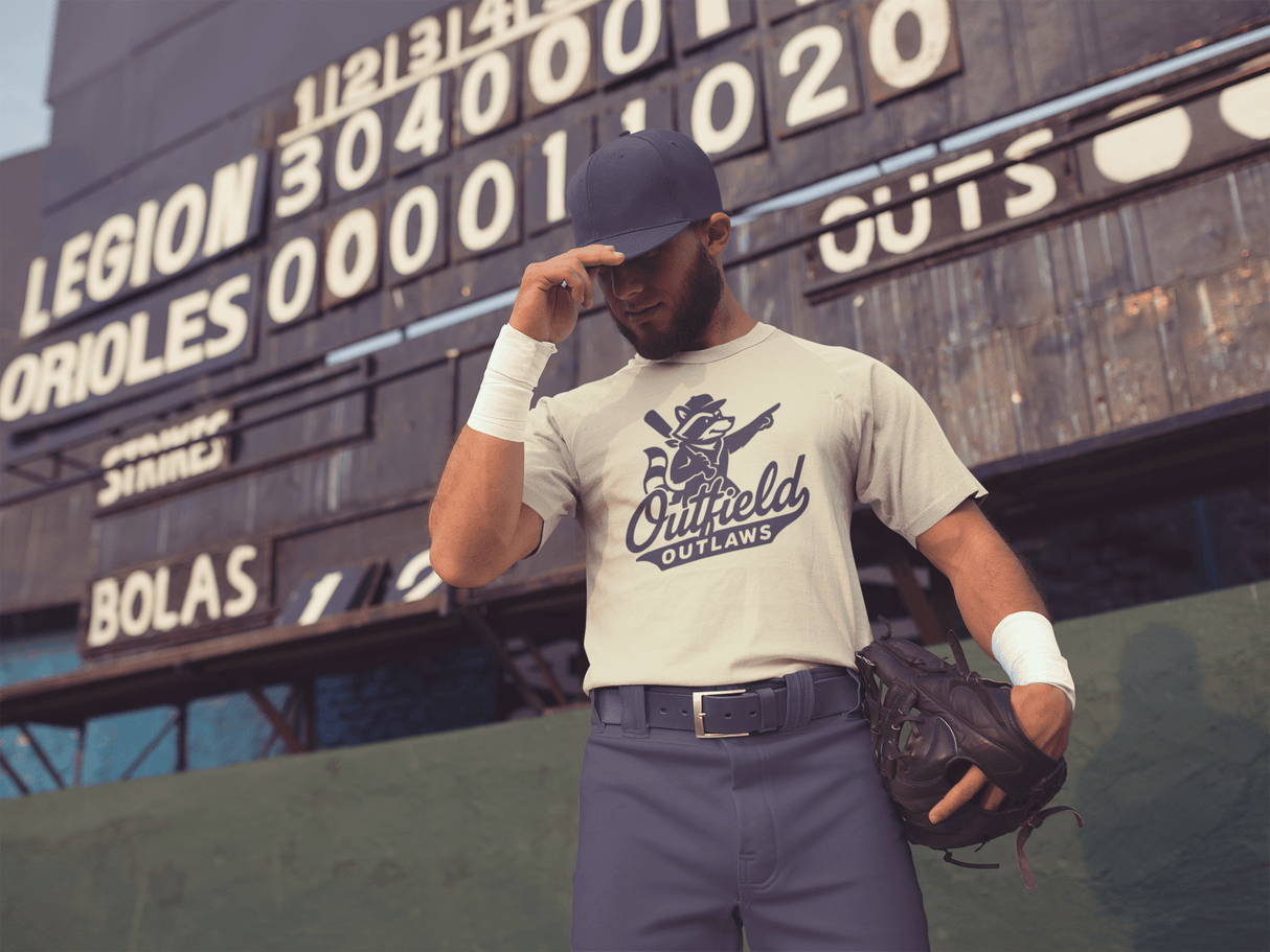 Baseball player wearing Outfield Outlaws logo t-shirt in vintage white, standing in front of an old-school scoreboard, Bella Canvas tee