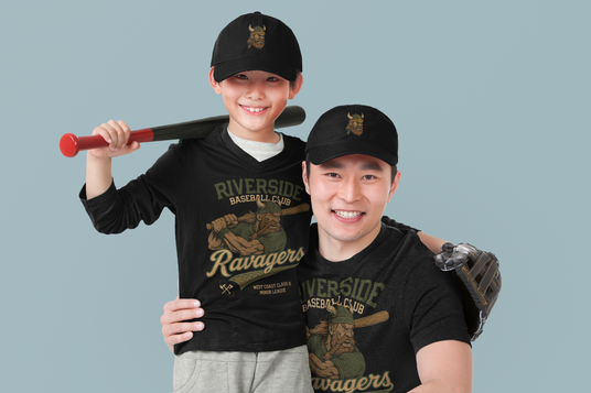 Father and son smiling while wearing matching Riverside Ravagers t-shirts and black hats featuring the Bjorn the Basher Viking mascot.