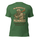 Flat lay of McMinnville Mummies retro baseball t-shirt in heather grass green, showcasing vintage mummy mascot and distressed design.
