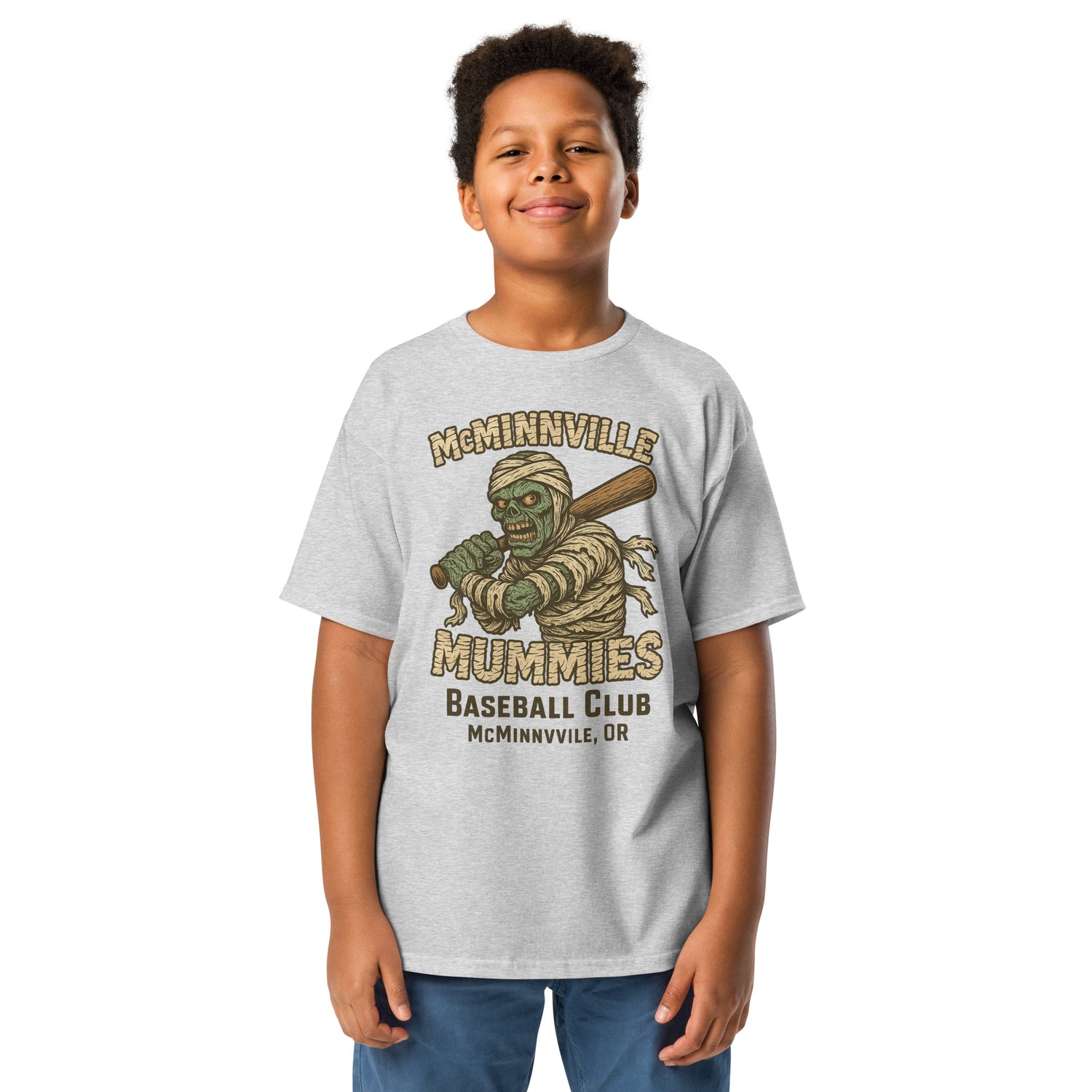 Young boy wearing McMinnville Mummies youth retro baseball t-shirt in athletic heather with vintage mummy mascot and classic minor league style.