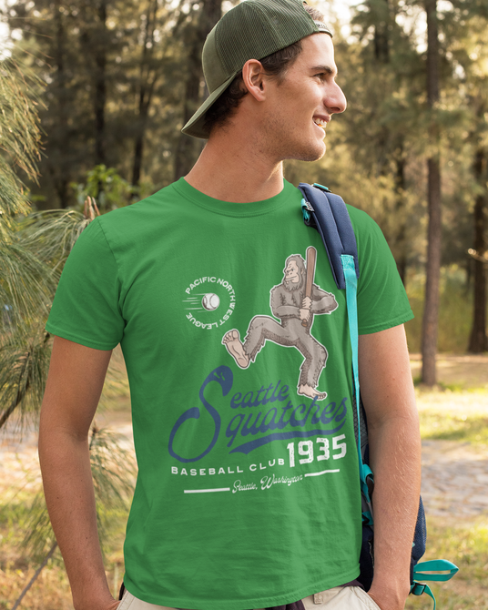 Man wearing a green Seattle Squatches vintage baseball t-shirt featuring the Boone Dinger mascot while hiking through a wooded forest trail.