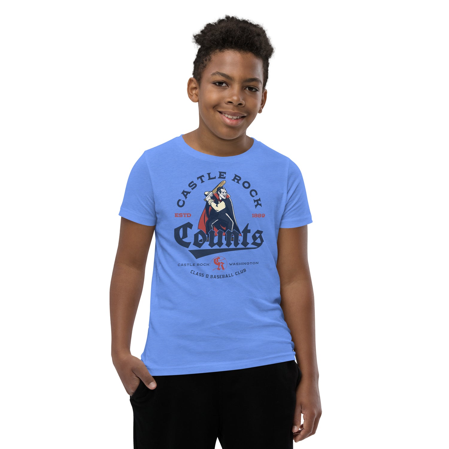 Young boy wearing Heather Columbia Blue Castle Rock Counts retro baseball shirt featuring a vampire-themed minor league mascot design.