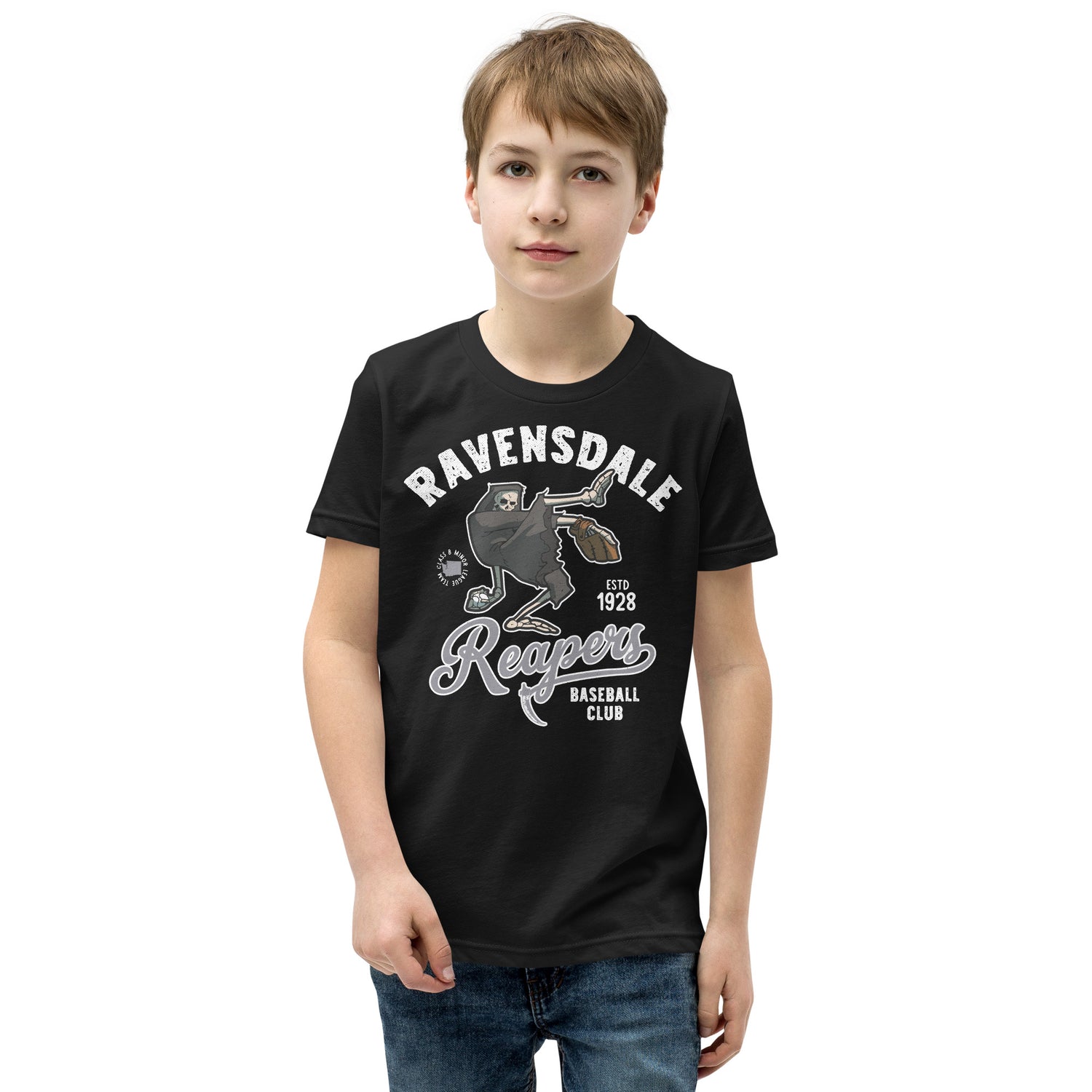 Young boy modeling the Ravensdale Reapers youth baseball t-shirt in black, featuring a vintage grim reaper mascot from a fictional minor league team.